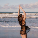 Model am Strand tanzend von hinten mit kurzem transparenten Negligee und Schnürung