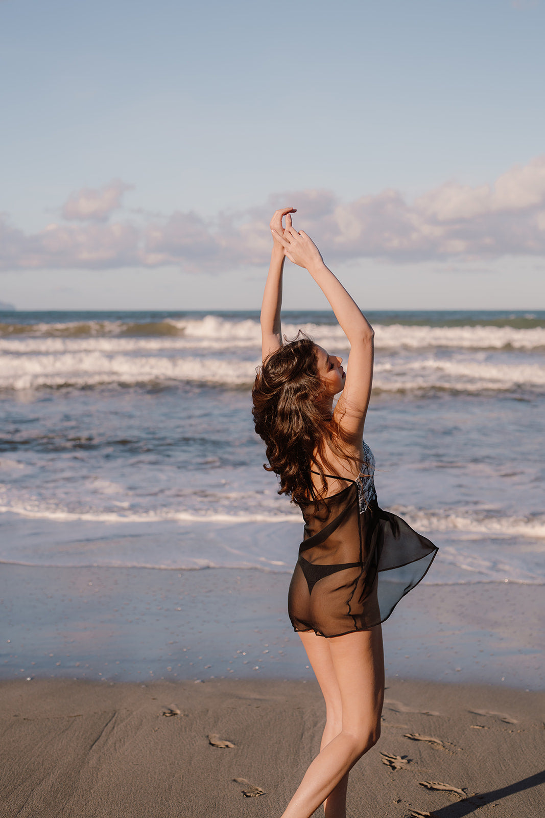 Model am Strand tanzend von hinten mit kurzem transparenten Negligee und Schnürung