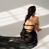 Moderne Göttin sitzt auf dem Boden und trägt langes sexy elegantes Negligé mit Taillenband in schwarz. Perspektive ist auf dem Rücken